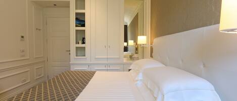 A hotel room with a neatly made bed, a wardrobe, a vanity with a mirror, and a lamp on the nightstand.