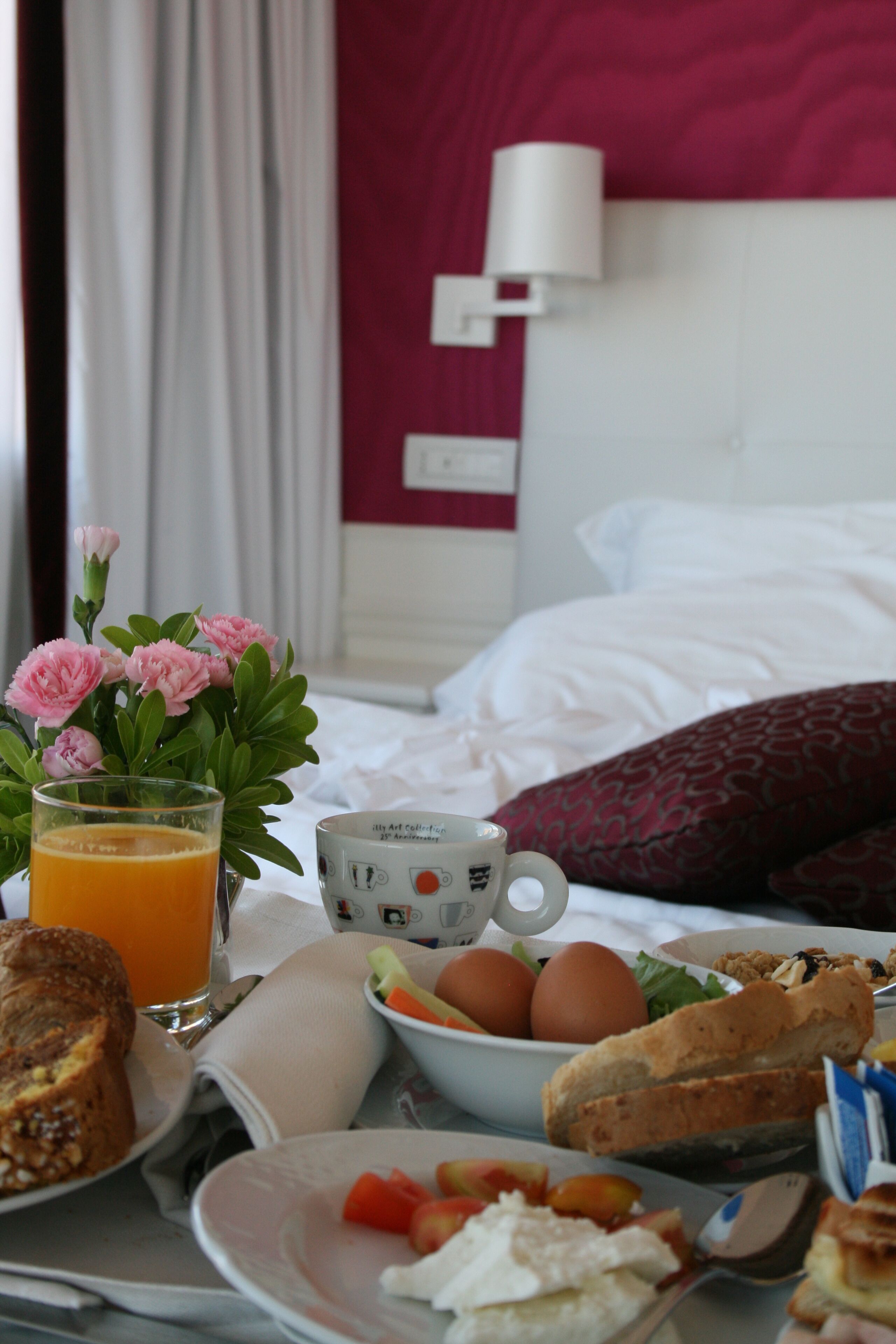 A breakfast table with a glass of orange juice, a mug, eggs, toast, and a bowl of fruit.
