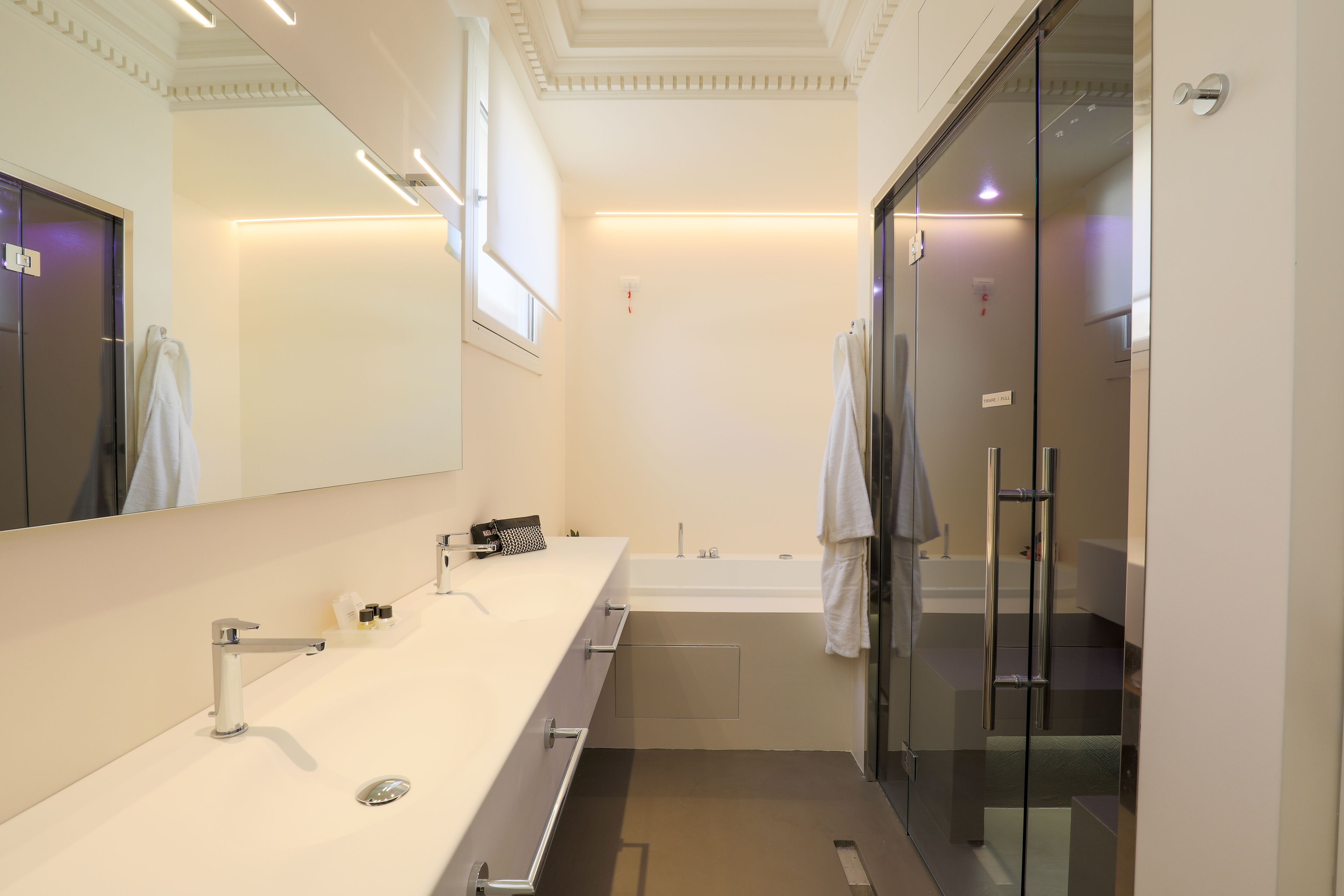 Un baño moderno con un espejo grande, un lavamanos blanco y una cabina de ducha de vidrio.
