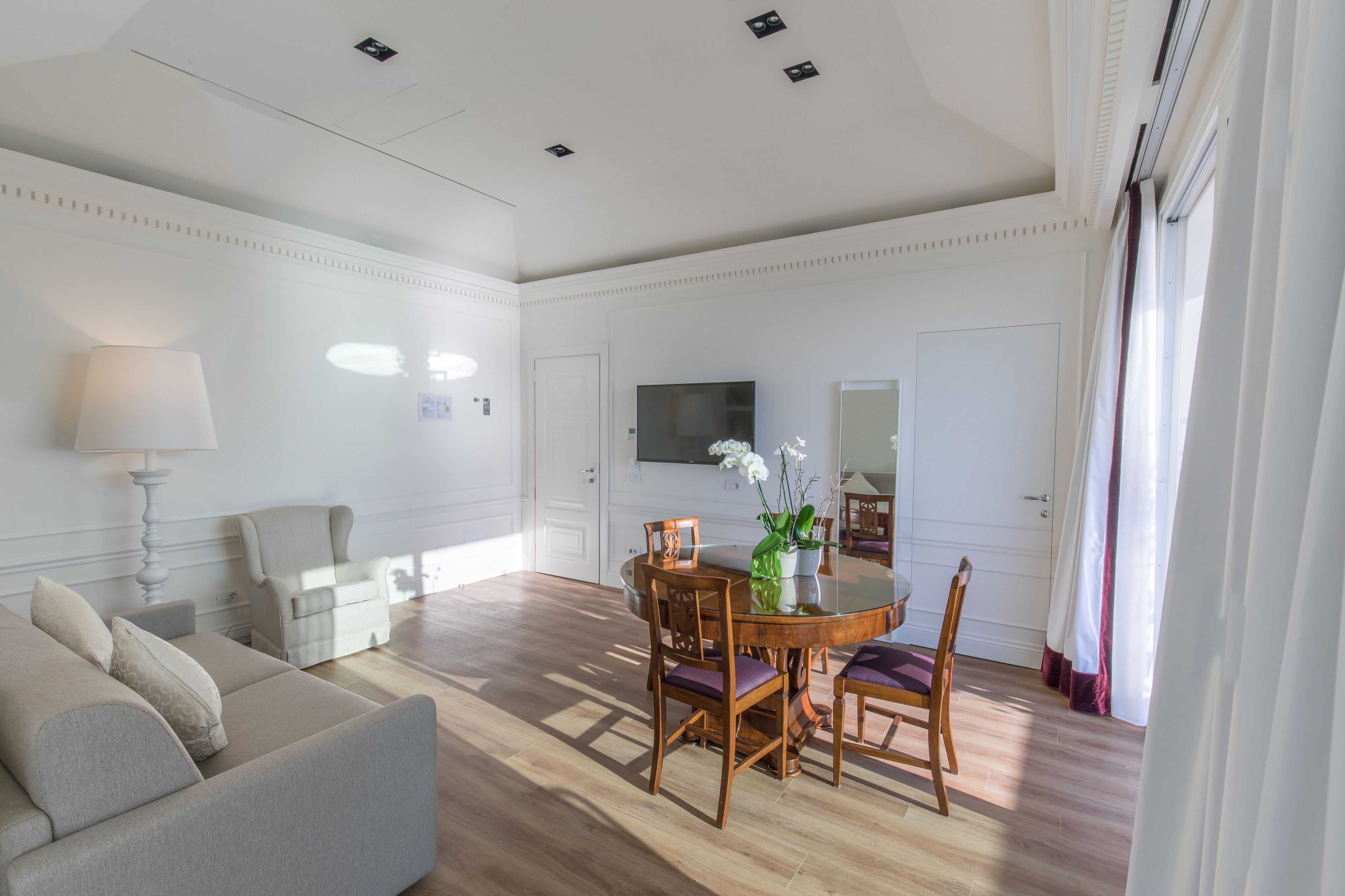 A spacious living room with a round wooden dining table, a sofa, and a TV mounted on the wall.
