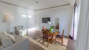 A spacious living room with a round wooden dining table, a sofa, and a TV mounted on the wall.