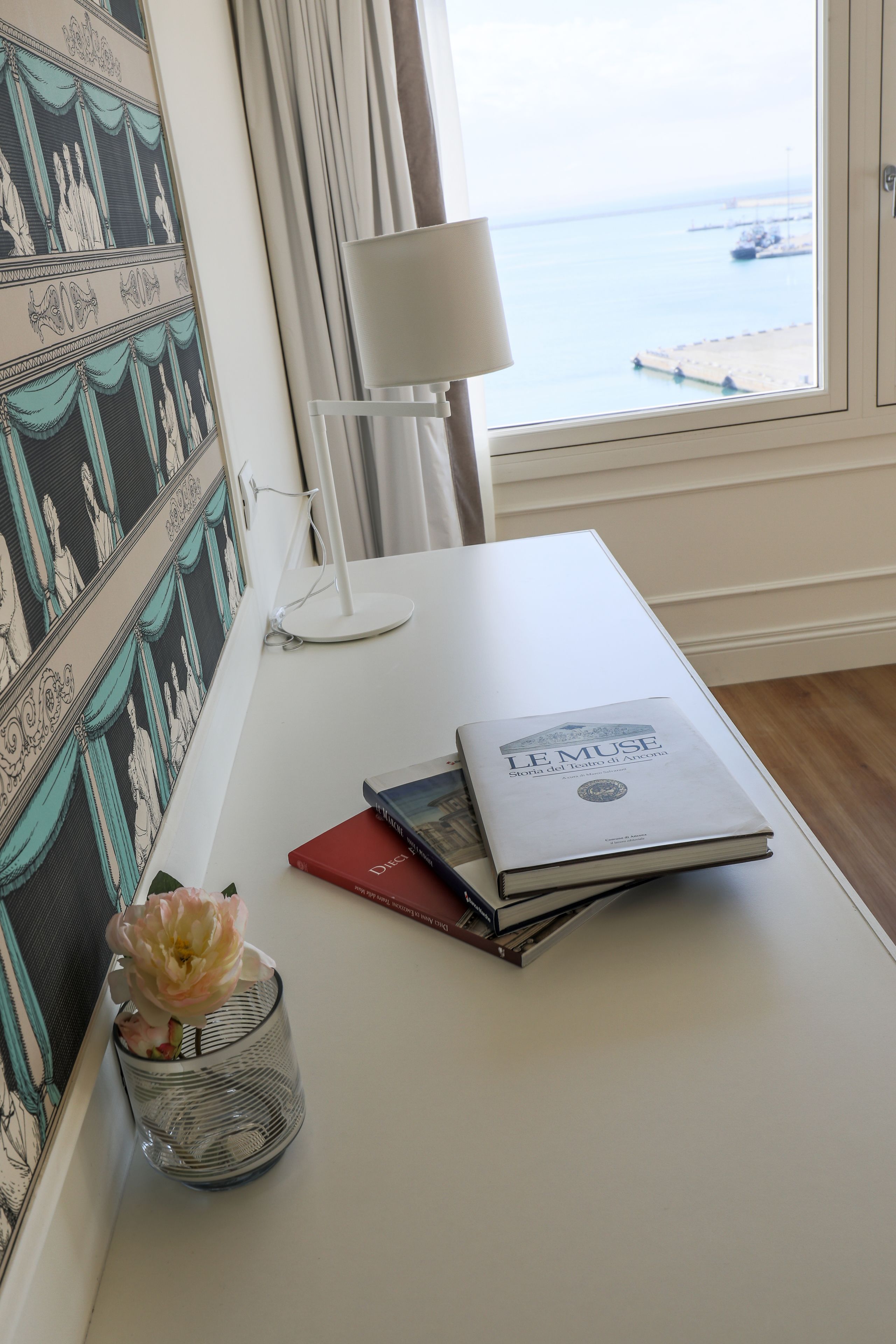 A desk with a book titled "LE MUSE," a lamp, and a vase with flowers.
