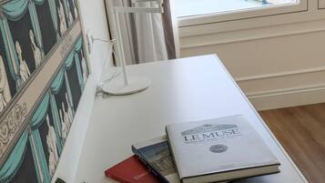 A desk with a book titled "LE MUSE," a lamp, and a vase with flowers.