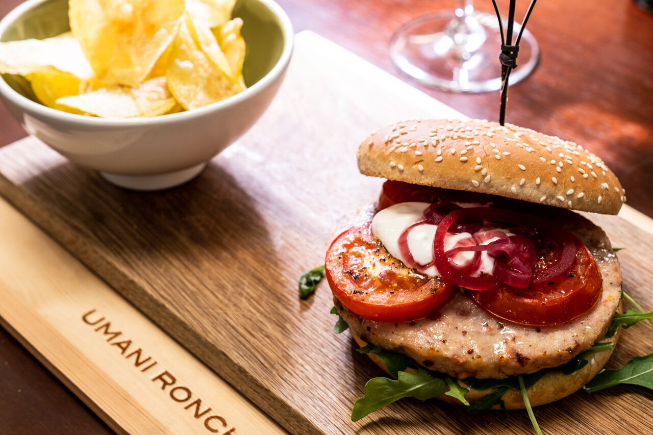 A burger with a sesame seed bun, tomato slices, and a side of chips.