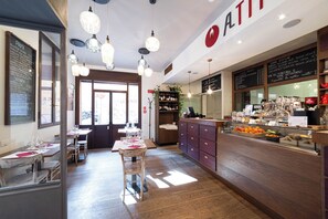 A restaurant interior with wooden tables, hanging pendant lights, and a counter with food and drink displays. -  Phi Hotel Bologna (Bologna)
