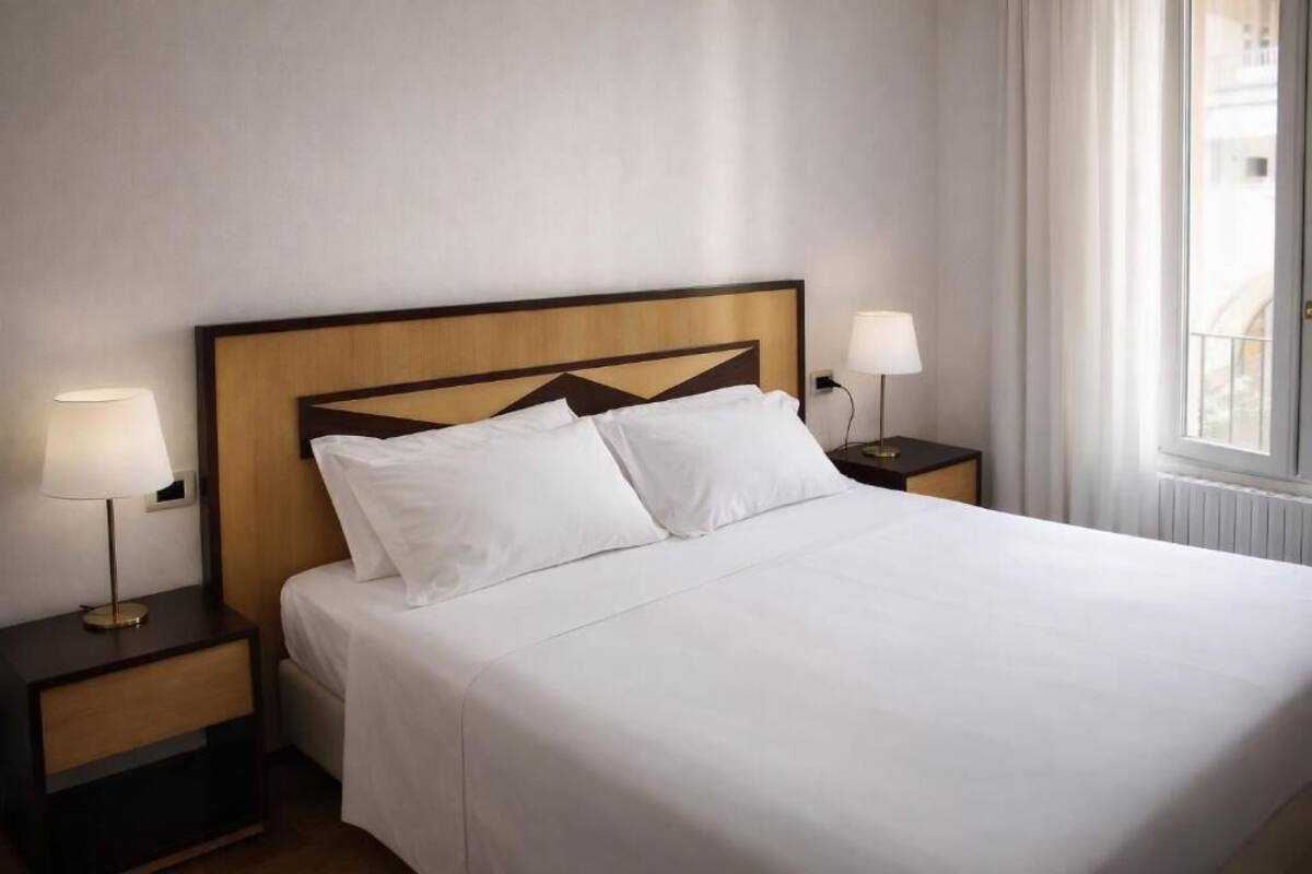Une chambre d’hôtel avec un grand lit, deux tables de chevet avec des lampes et une fenêtre avec des rideaux.