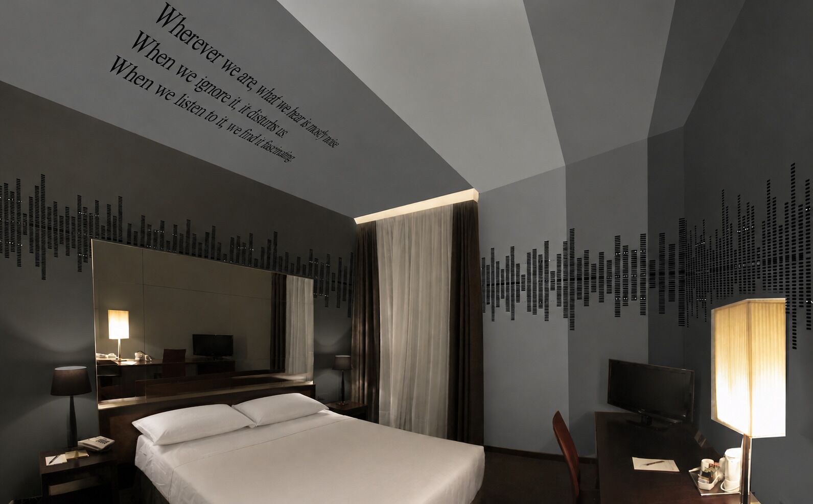A modern hotel room with a large bed, a desk with a chair, a television, and a mirror.