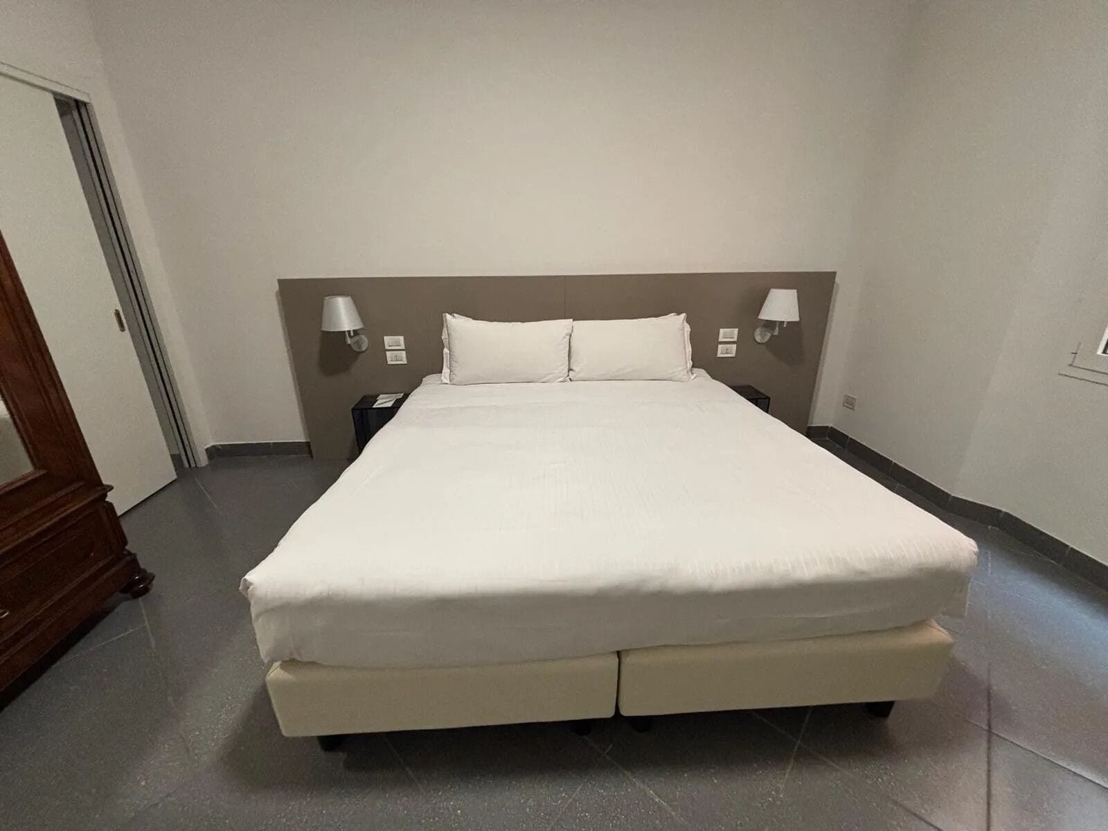Una cama grande con cabecera, dos mesitas de noche y lámparas fijadas a la pared.