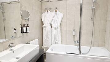 Een moderne badkamer met een groot wastafel, een badkuip en een douche. Twee witte badjassen hangen aan haken.