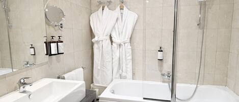 A modern bathroom with a large sink, a bathtub, and a shower. There are two white robes hanging on hooks.