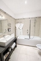 Een moderne badkamer met een groot wastafel, een badkuip en een douche. Twee witte badjassen hangen aan haken.