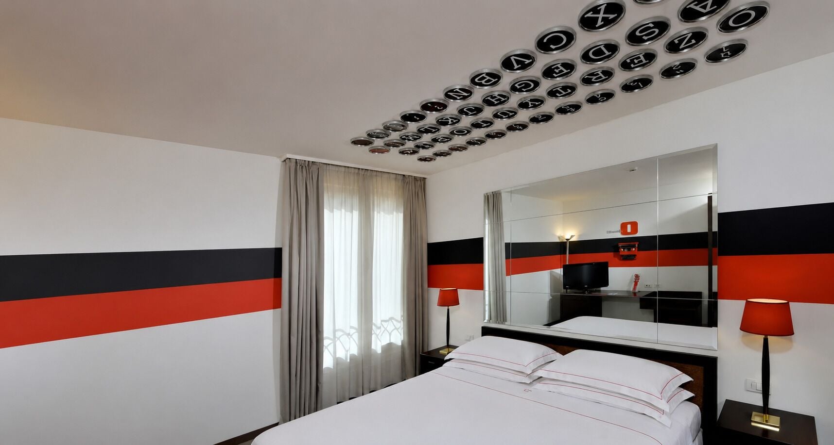 Une chambre d’hôtel avec un lit, un grand miroir, une télévision et un plafond orné de motifs circulaires.