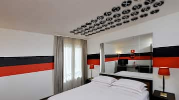 Une chambre d’hôtel avec un lit, un grand miroir, une télévision et un plafond orné de motifs circulaires.