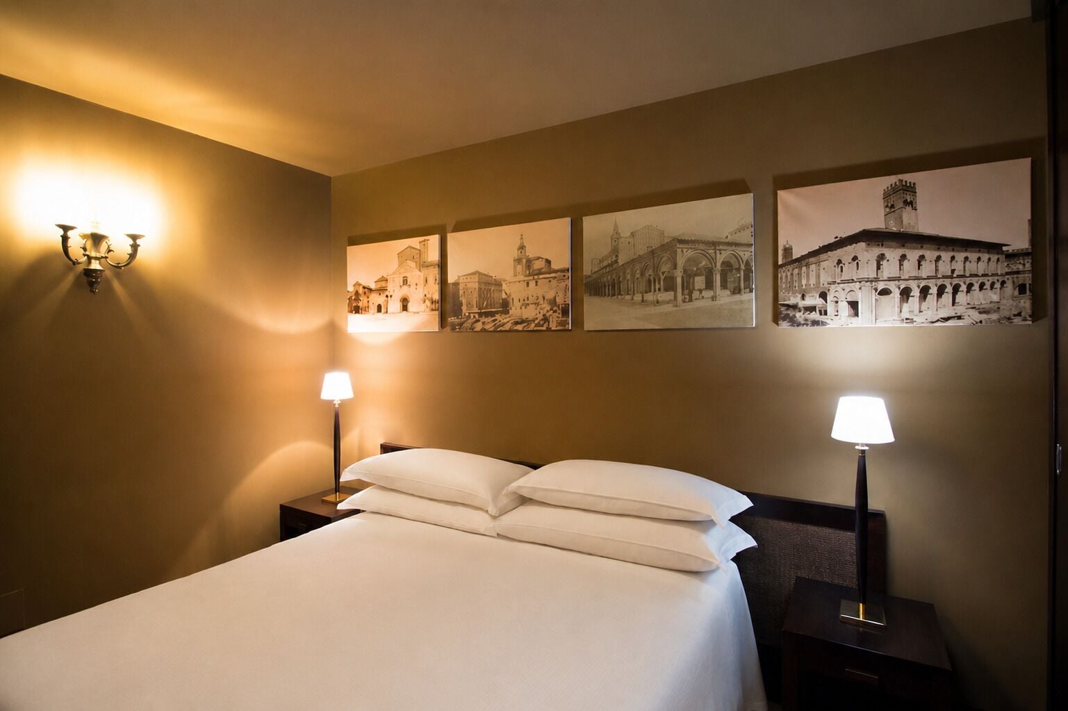 Una habitación de hotel con una cama, dos lámparas de noche y cuatro cuadros en la pared.
