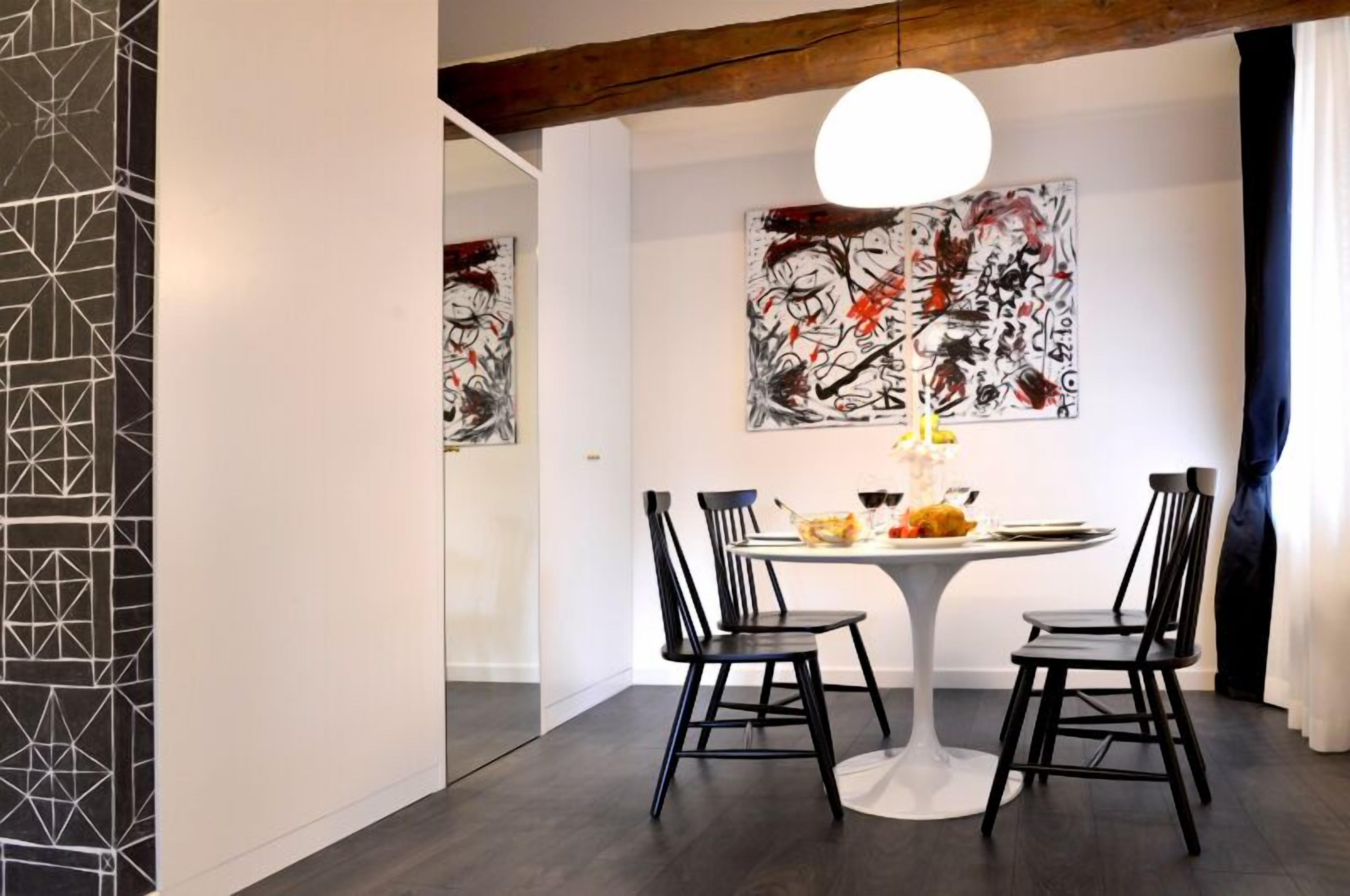 A dining area with a round table, four black chairs, and two abstract paintings on the wall.
