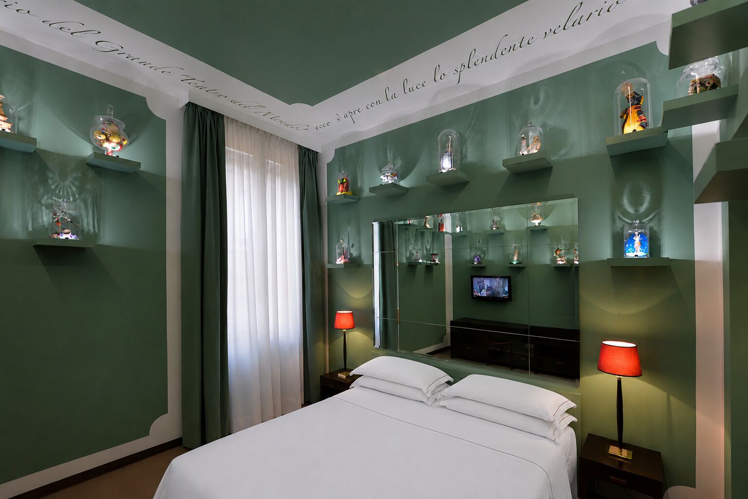 Quarto de hotel com cama, duas mesas de cabeceira, televisão e objetos decorativos nas prateleiras.