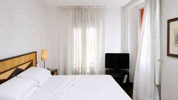 A hotel room with a bed, a TV, a nightstand, and a door.
