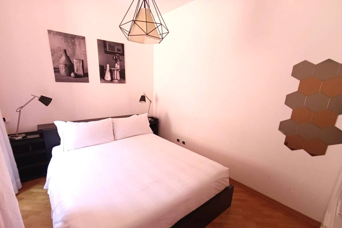 Une chambre à coucher comprenant un lit, deux lampes de chevet, un luminaire hexagonal fixé au mur et deux tableaux encadrés accrochés au mur.