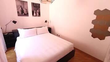 A bedroom with a bed, two bedside lamps, a wall-mounted hexagonal light fixture, and two framed pictures on the wall.