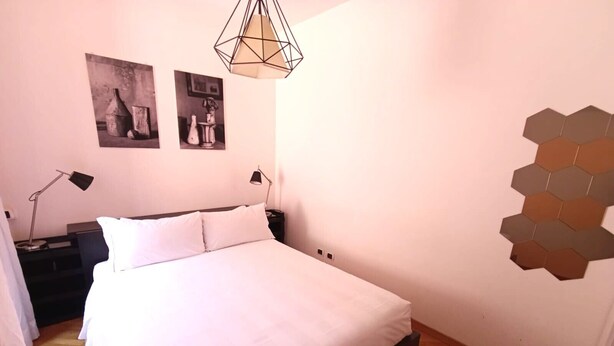Ein Schlafzimmer mit einem Bett, zwei Nachttischlampen, einer sechseckigen Wandleuchte und zwei gerahmten Bildern an der Wand.