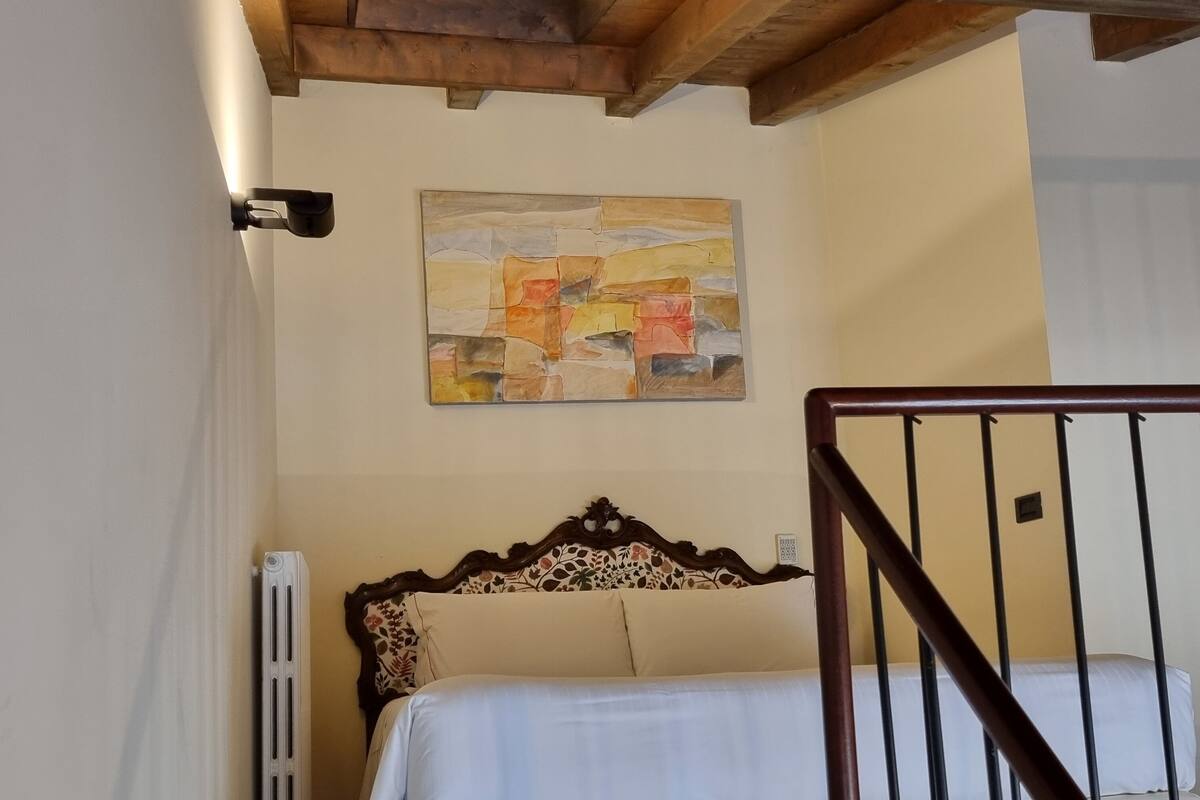 Une chambre à coucher avec une tête de lit en bois, un lit avec une literie blanche, un radiateur et un tableau accroché au mur.