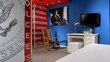 Un dormitorio moderno con una pared azul de acento, un televisor montado, un escritorio con silla y una cama grande.