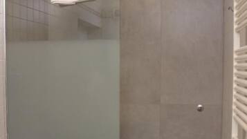 Een moderne badkamer met een glazen douchecabine, een witte wasbak en een handdoekhouder.