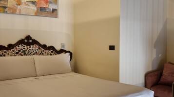 A bedroom with a bed, a floral-patterned headboard, a painting on the wall, and a window with blinds.