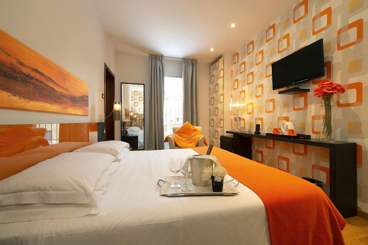 A hotel room with a bed, a TV, a desk, and a window.