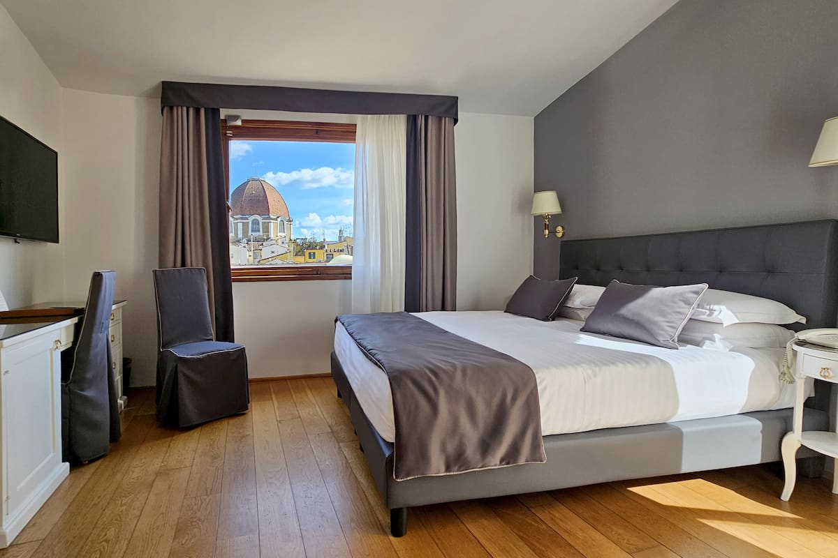 A bedroom with a bed, a chair, a desk, a lamp, and a view of a dome building.