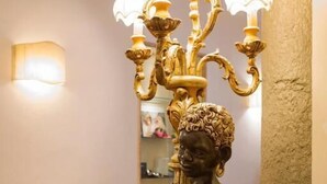 A statue of a woman with a draped cloth, a chandelier with multiple lights, and a beige sofa in a room with a tiled floor. - Hotel Atlantic Palace (Florence)
