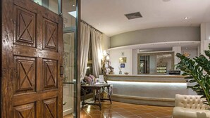 A hotel lobby with a reception desk, a wooden door, a white armchair, and a tiled floor. - Hotel Atlantic Palace (Florence)