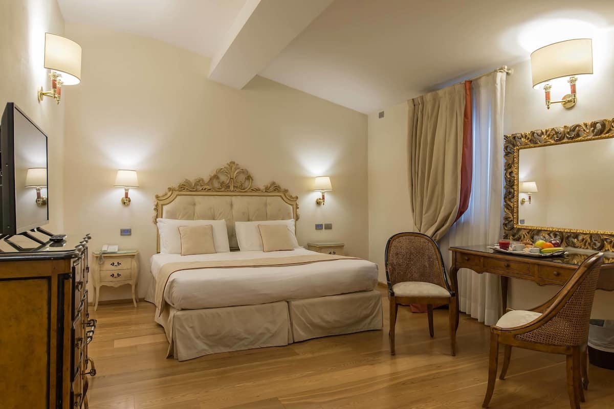 A hotel room with a large bed, bedside lamps, a desk with a chair, and a mirror.