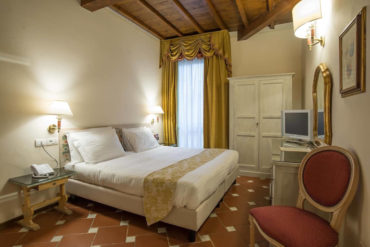 A hotel room with a bed, bedside lamps, a television, a chair, and a wardrobe.