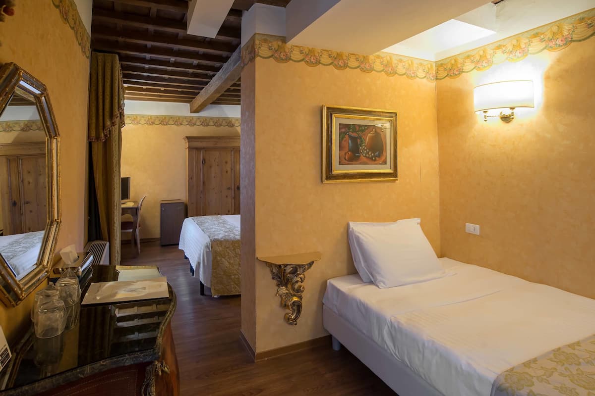 A hotel room with a wooden ceiling, a bed with white linens, a bedside table, a mirror, and a wall-mounted lamp.
