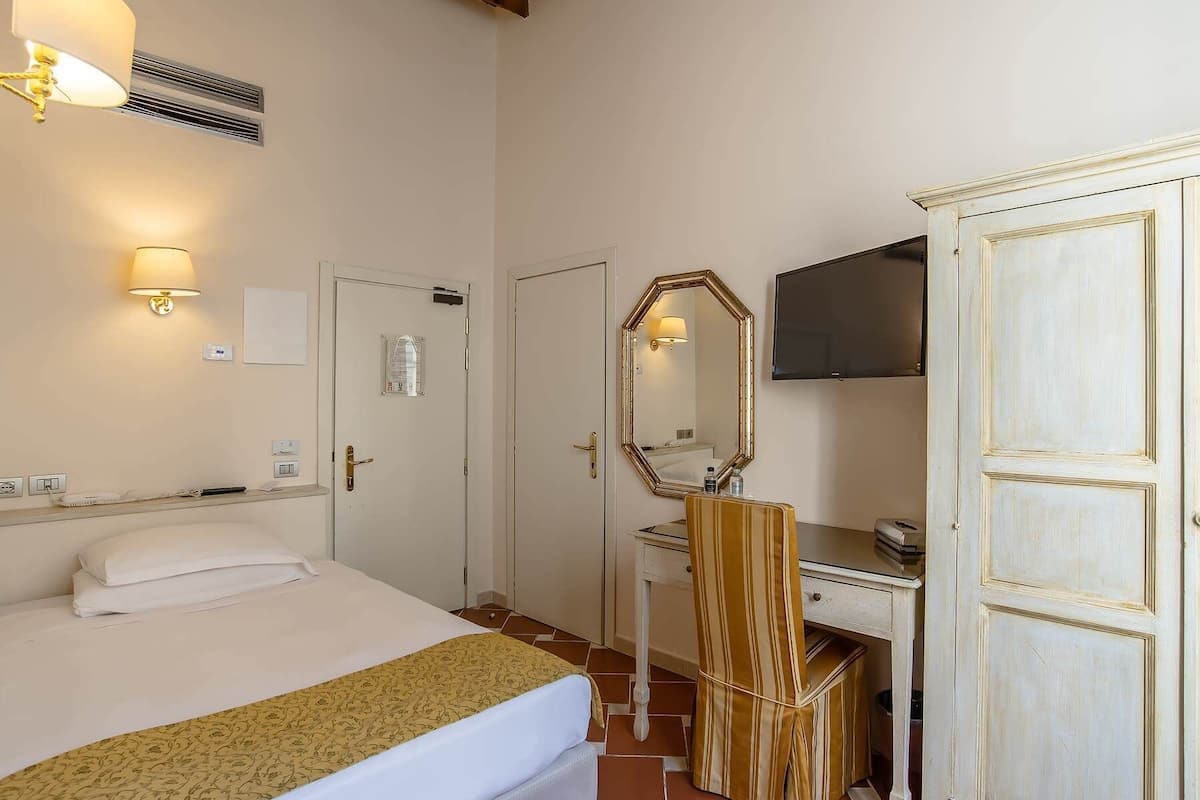 A hotel room with a bed, a desk with a mirror, a television, and a wardrobe.