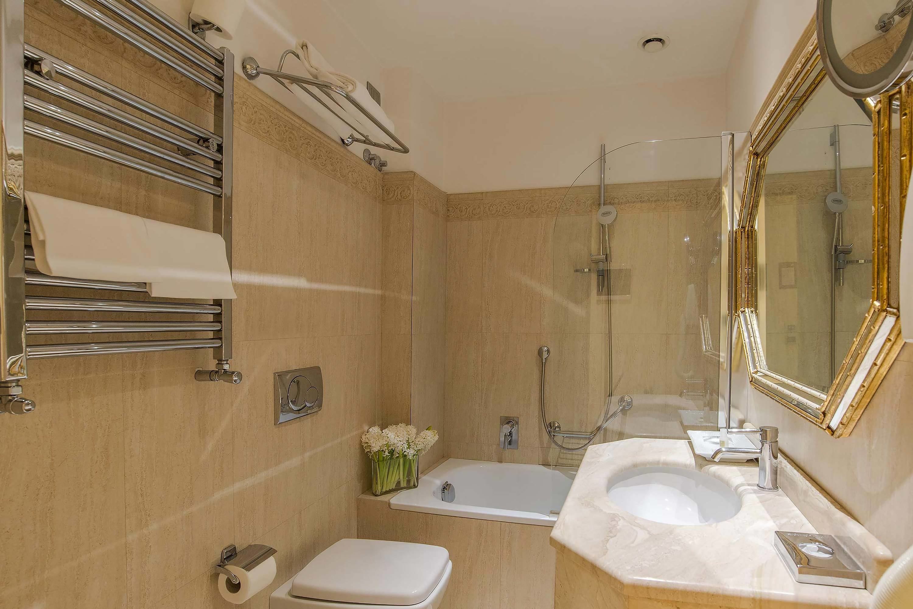 A bathroom with a bathtub, toilet, and sink, featuring a mirror, towel rack, and a vase of flowers.