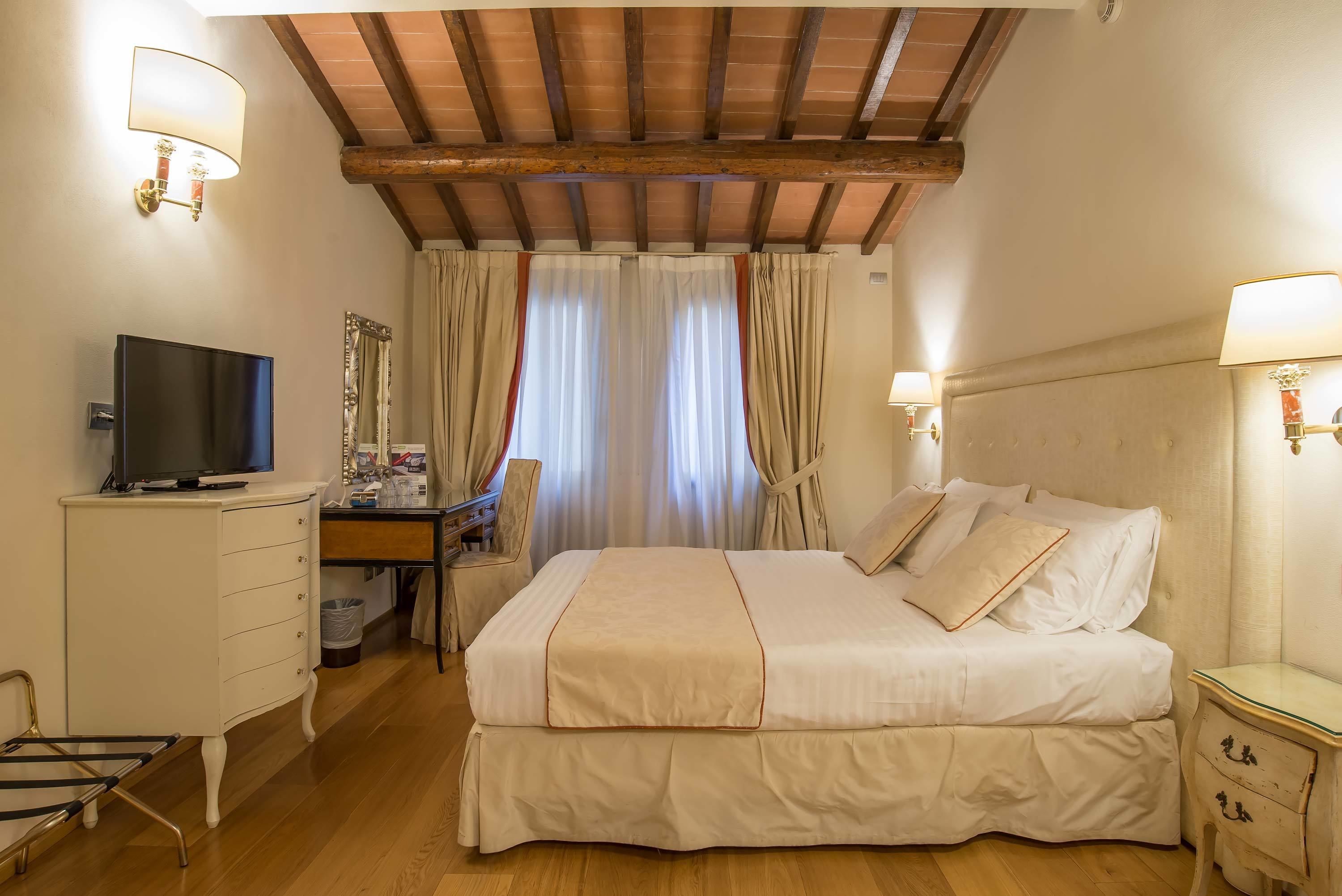 A bedroom with a bed, bedside tables, a desk, a television, and curtains.