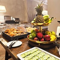 Una mesa de buffet con diversas opciones de comida, como frutas, pasteles y pepinos en rodajas.