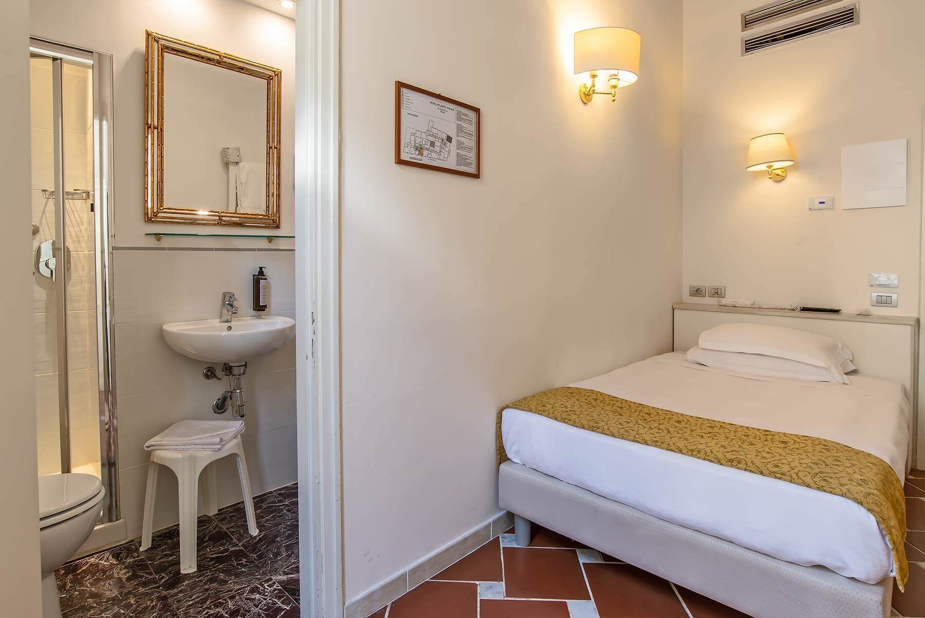Una habitación de hotel con una cama, una mesita de noche, un lavabo y un espejo.