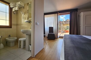 Habitación de hotel con cama, baño con lavamanos, bidé y espejo. Hay una ventana con cortinas y vista al exterior.