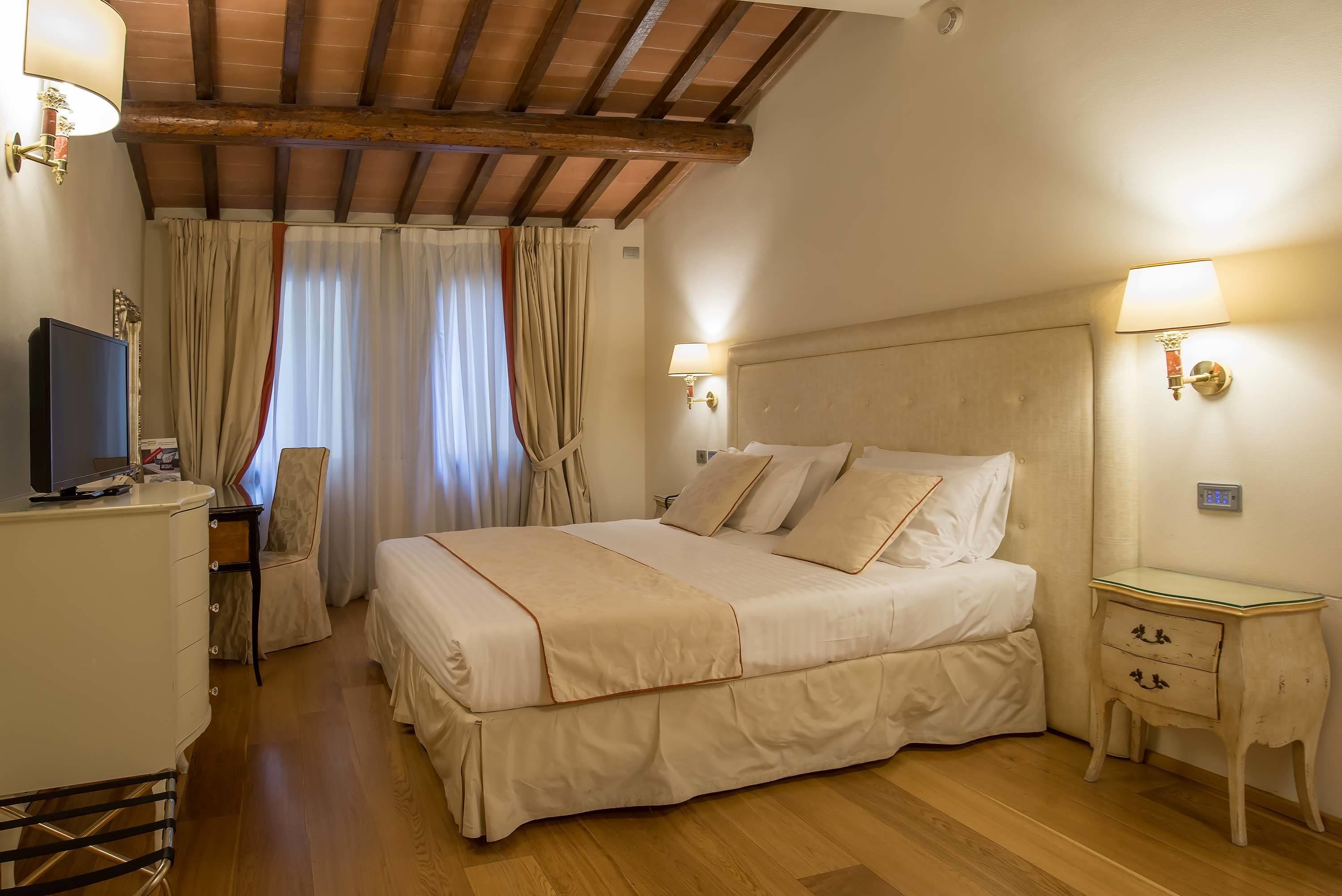 Hotelkamer met een groot bed, bedlampjes, een bureau met lamp, een stoel en een televisie.