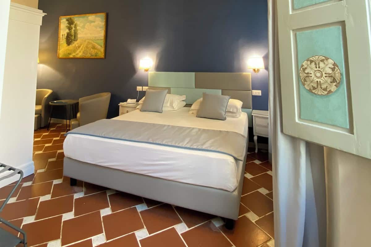 A bedroom with a large bed, a nightstand, a chair, and a painting on the wall.