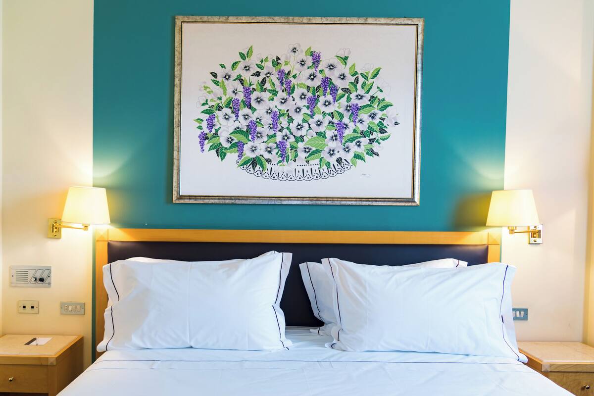 Ein Hotelzimmer mit einem Bett, zwei Nachttischen, einer Lampe und einem floralen Bild an der Wand.
