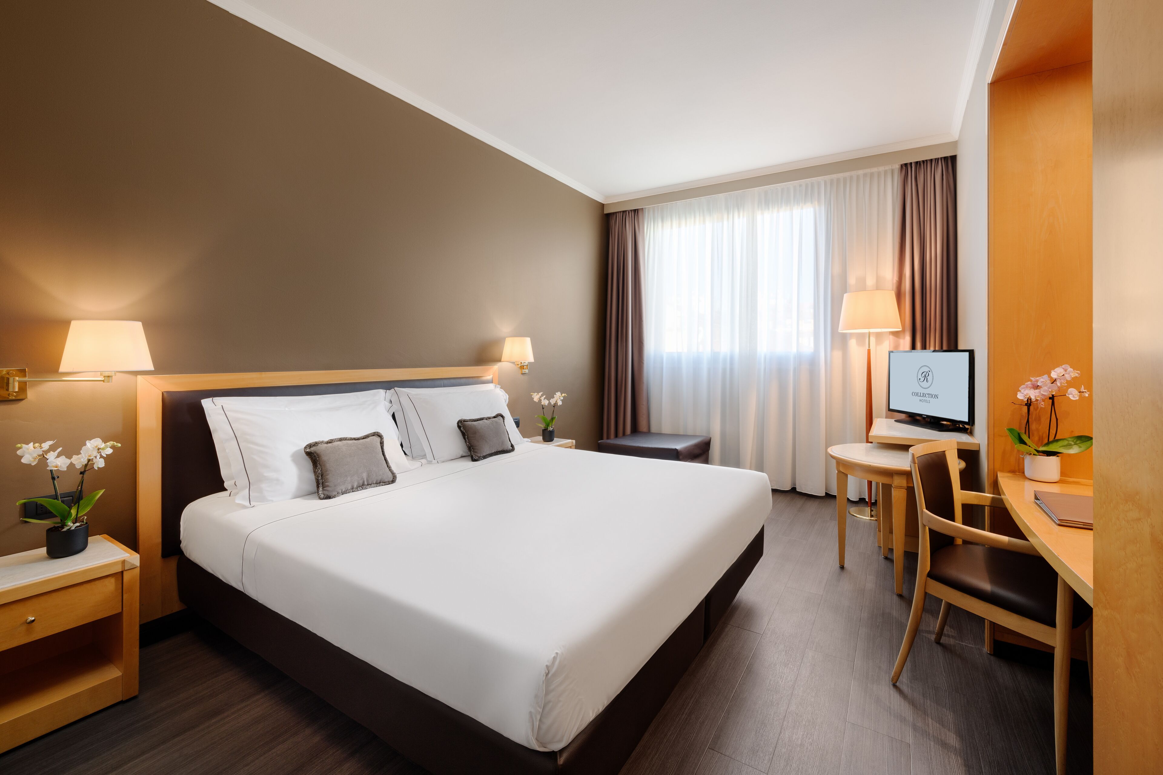 A hotel room with a large bed, bedside tables with lamps, a desk with a chair, and a television.