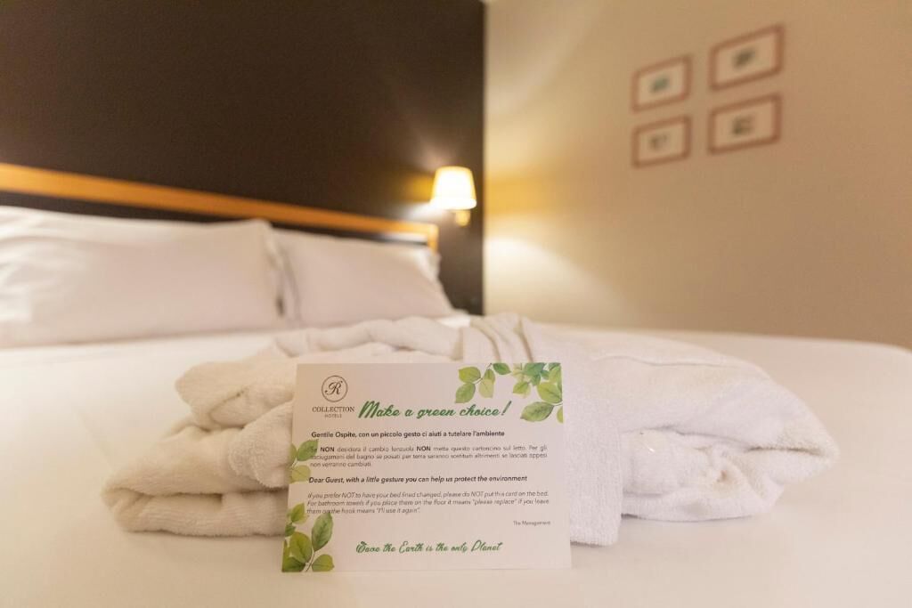 A neatly made bed with a folded white towel and a card on it.