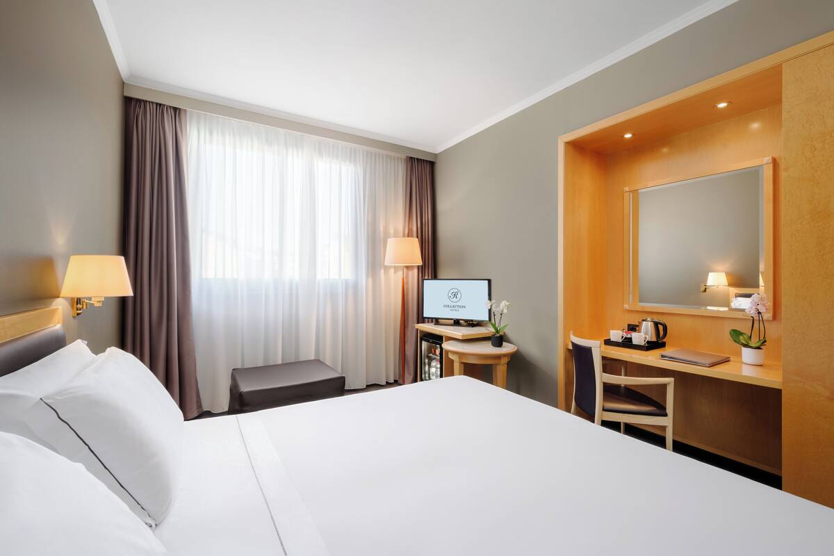 Ein Hotelzimmer mit Bett, Schreibtisch, Stuhl, Lampe und Fernseher.