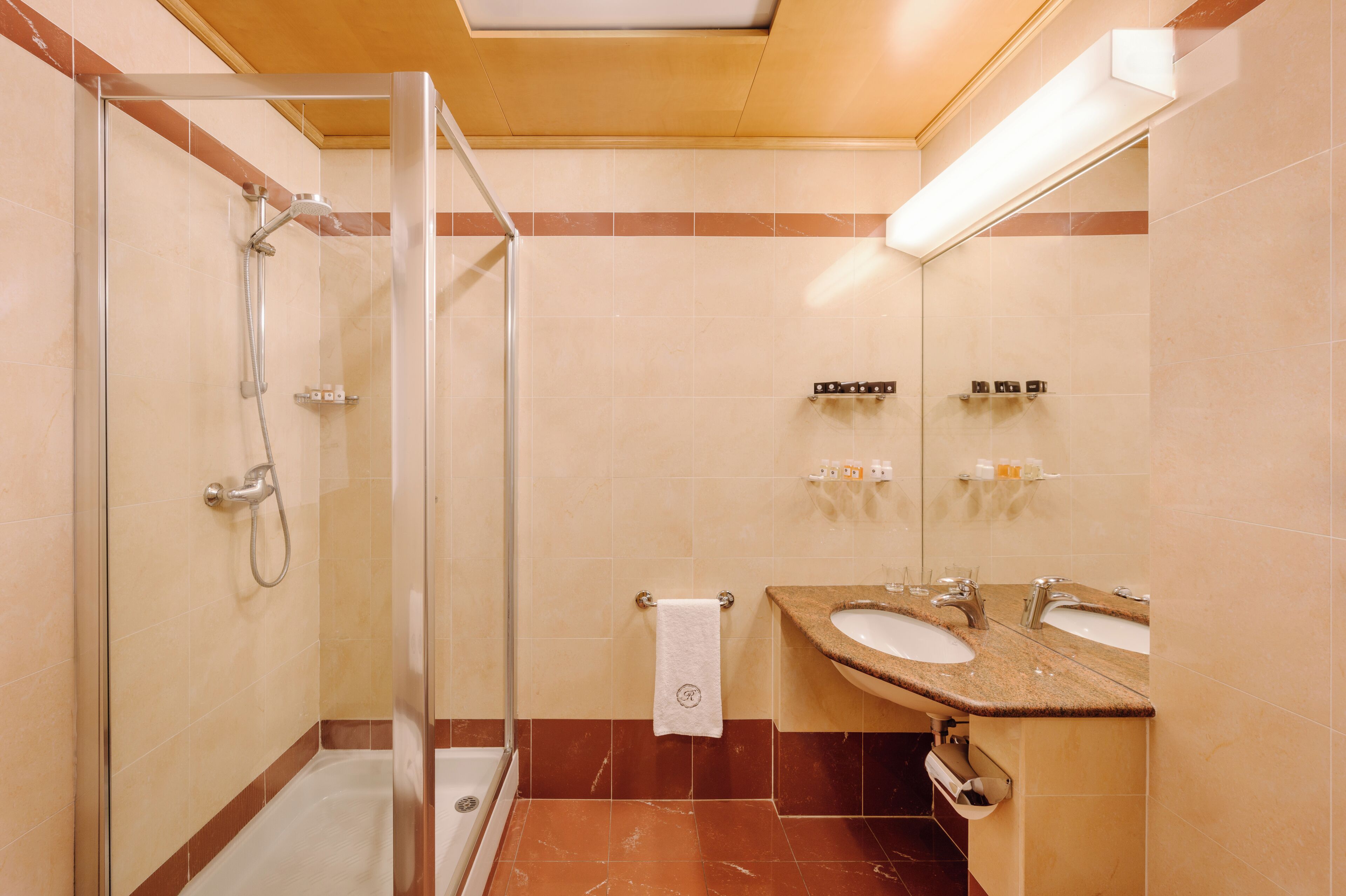 A bathroom with a glass-enclosed shower, two sinks, and a towel rack.