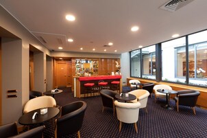 Una hall d'albergo con area bar, posti a sedere e ampie finestre che lasciano entrare la luce naturale.