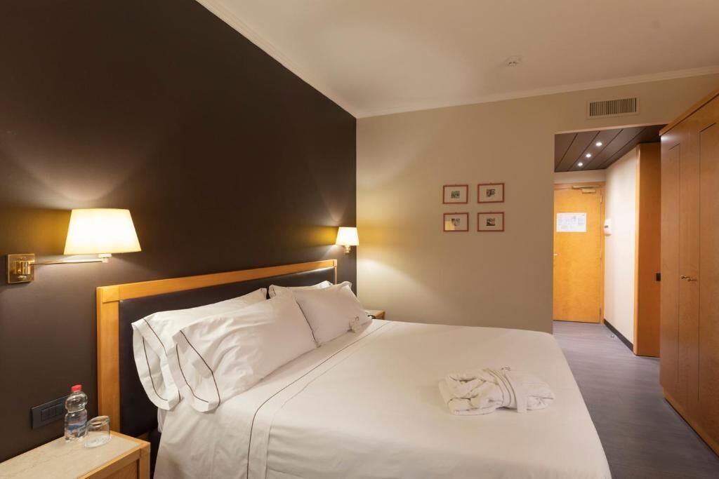 A hotel room with a bed, bedside lamps, a nightstand, and a wardrobe.